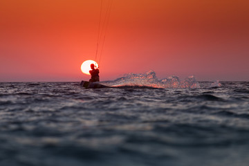 Silhouette of a kitesurfer sailing at sunset over the sun