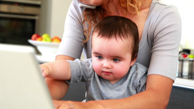 Mother sitting with baby son on lap using laptop