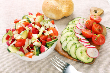 Salad with fresh vegetables in white bowl with rolls