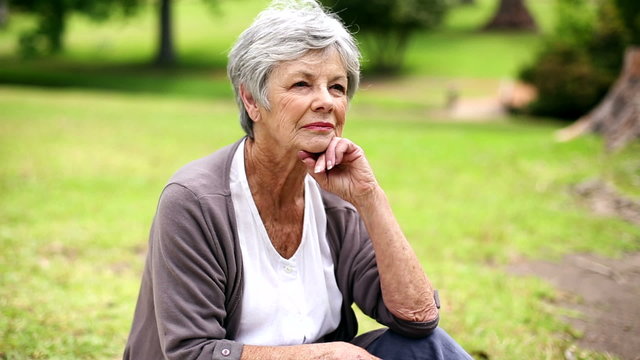 Upset senior woman sitting in the park thinking