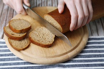 Female hands cutting bread on wooden board, close-up