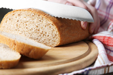 Female hands cutting bread on wooden board, close-up