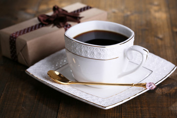 Cup of coffee and gift on wooden table close-up