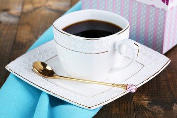Cup of coffee and gift on wooden table close-up