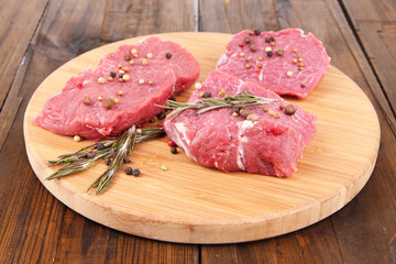 Raw beef meat with spices on cutting board on wooden background