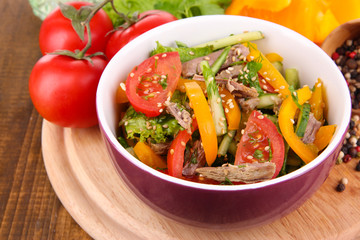 Beef salad in bowl with vegetables and spices on wooden table