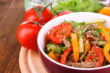 Beef salad in bowl with vegetables on wooden background