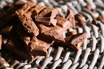 Chopped bar of chocolate on wicker mat background