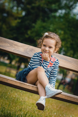 Cute little girl sitting on the bench in a park