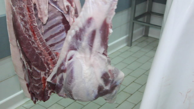 Butcher cutting hanging pork meat in a butchery