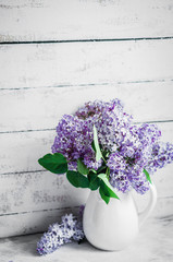 Lilacs in white vase on rustic background