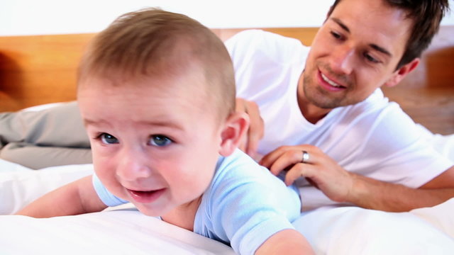 Happy father tickling his baby son on bed