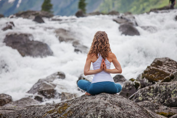 Young woman is practicing yoga at mountain river