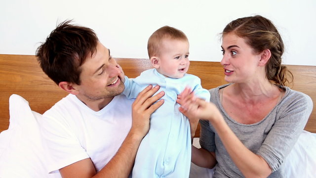 Happy parents lying on bed with baby son