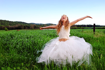 Cute girl with open arms in green grass field.