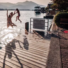 Muurstickers teenage girls jumping off a dock at lake © naatphoto