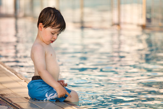 Cute toddler boy sitting by a swimming pool