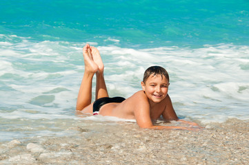 Fototapeta premium Boy at the sea lying on the sand and waves