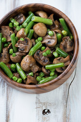 Wooden bowl with fried champignons, peas and beans, above view