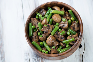 Roasted champignons with peas and beans in a bowl, above view