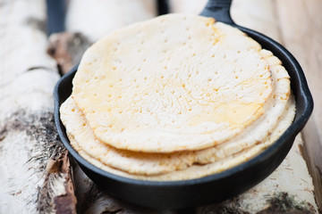 Frying pan with tortillas over wooden logs, horizontal shot