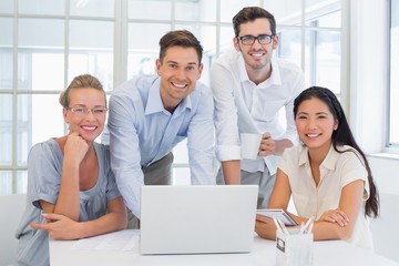 Casual business team smiling at camera together at desk