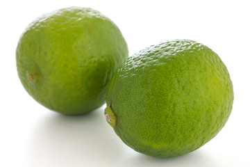 Two whole limes on a white surface
