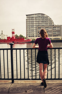 Young woman relaxing by river and looking across at buildings