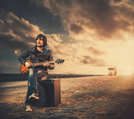 young man with guitar at sunset road