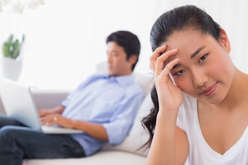 Upset woman sitting on couch while boyfriend uses laptop