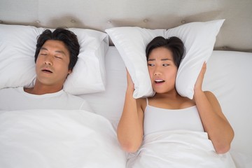 Annoyed woman covering her ears with pillows to block out snorin