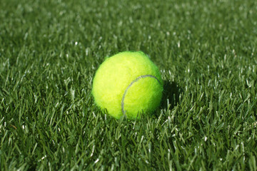 Yellow tennis ball lays on synthetic grass court closeup
