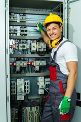Cheerful electrician in a safety hat on a factory - 64761328