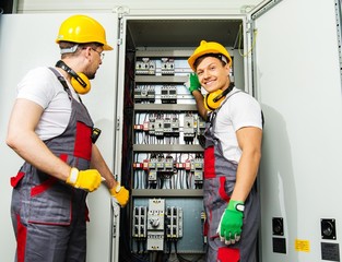 Two electricians in a safety hat and headphones on a factory