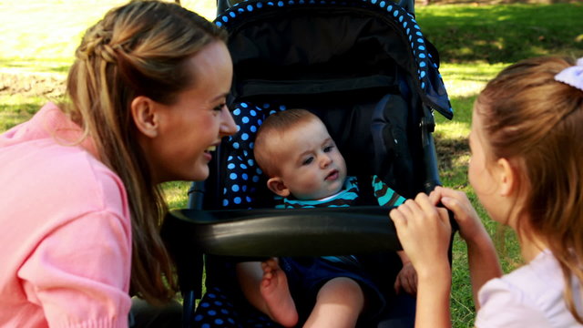 Mother and daughter playing with baby in a pram in the park