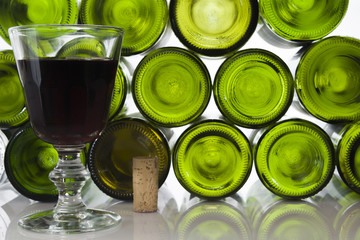 Rotweinglas mit Korken vor Weinflaschen vor weißem  Hintergrund