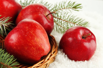 Red apples with fir branches on wicker stand on snow close up