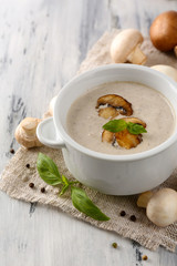 Mushroom soup in white pot, on napkin, on wooden background