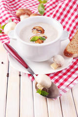 Mushroom soup in white pot, on napkin, on wooden background