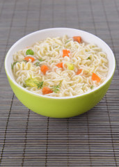 Tasty instant noodles with vegetables in bowl on table close-up
