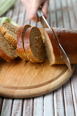 Female hands cutting bread on wooden board, close-up