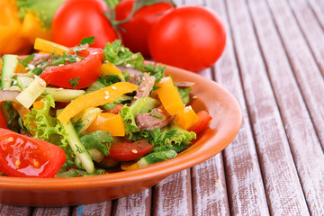 Beef salad on plate with vegetables on wooden background