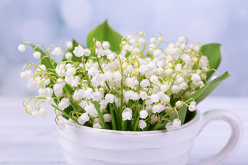 Beautiful lilies of the valley in cup on wooden table