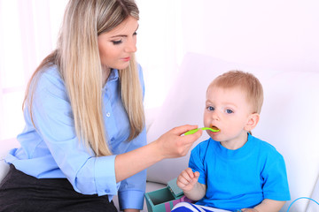 Young pretty mother feeding her son on sofa in room