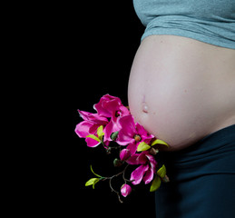 pregnant woman on black background with hands on her belly