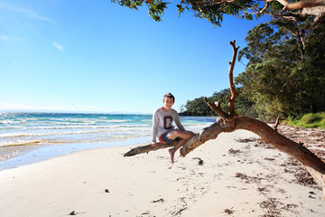 Cheerful teen boy sitting on tree  holiday at the beach Australi