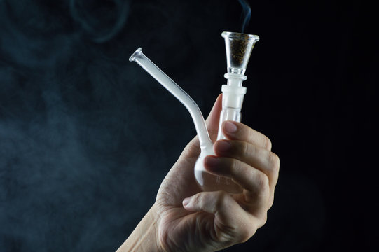 hand with a pipe and marijuana smoking on black