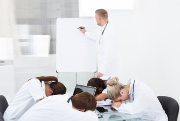 Doctor Giving Presentation To Colleagues Sleeping At Desk