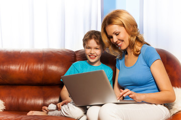 Fototapeta na wymiar Happy mum and son with laptop on the sofa