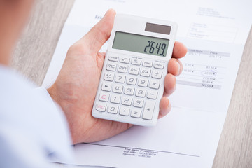 Businessman's Hands Calculating Invoice At Desk